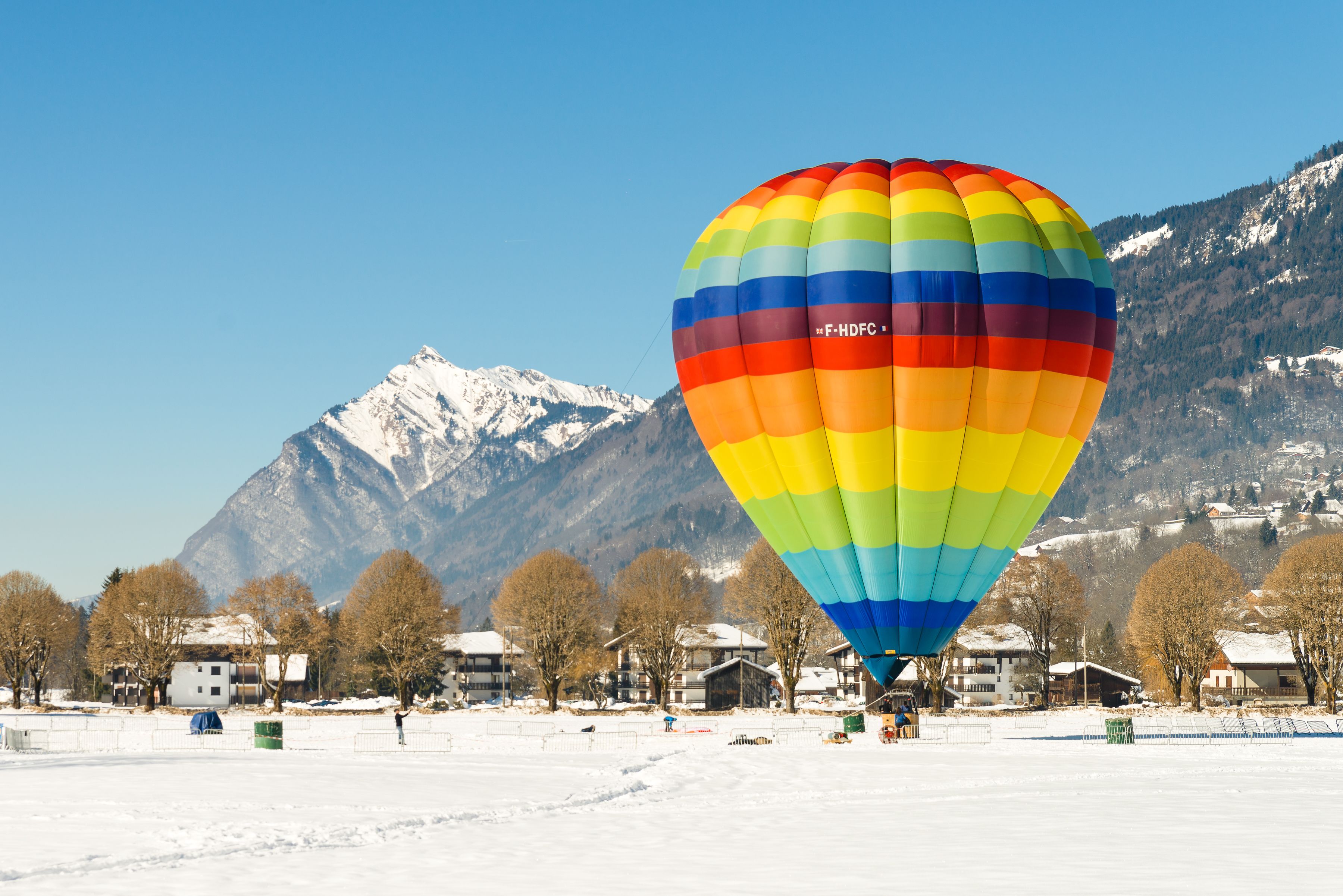 Eine farbenfrohe Heißluftballon in einer verschneiten Landschaft mit Bergen im Hintergrund.