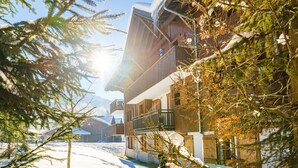 Een pad bedekt met sneeuw dat leidt naar een houten chalet met balkons, omringd door altijdgroene bomen.