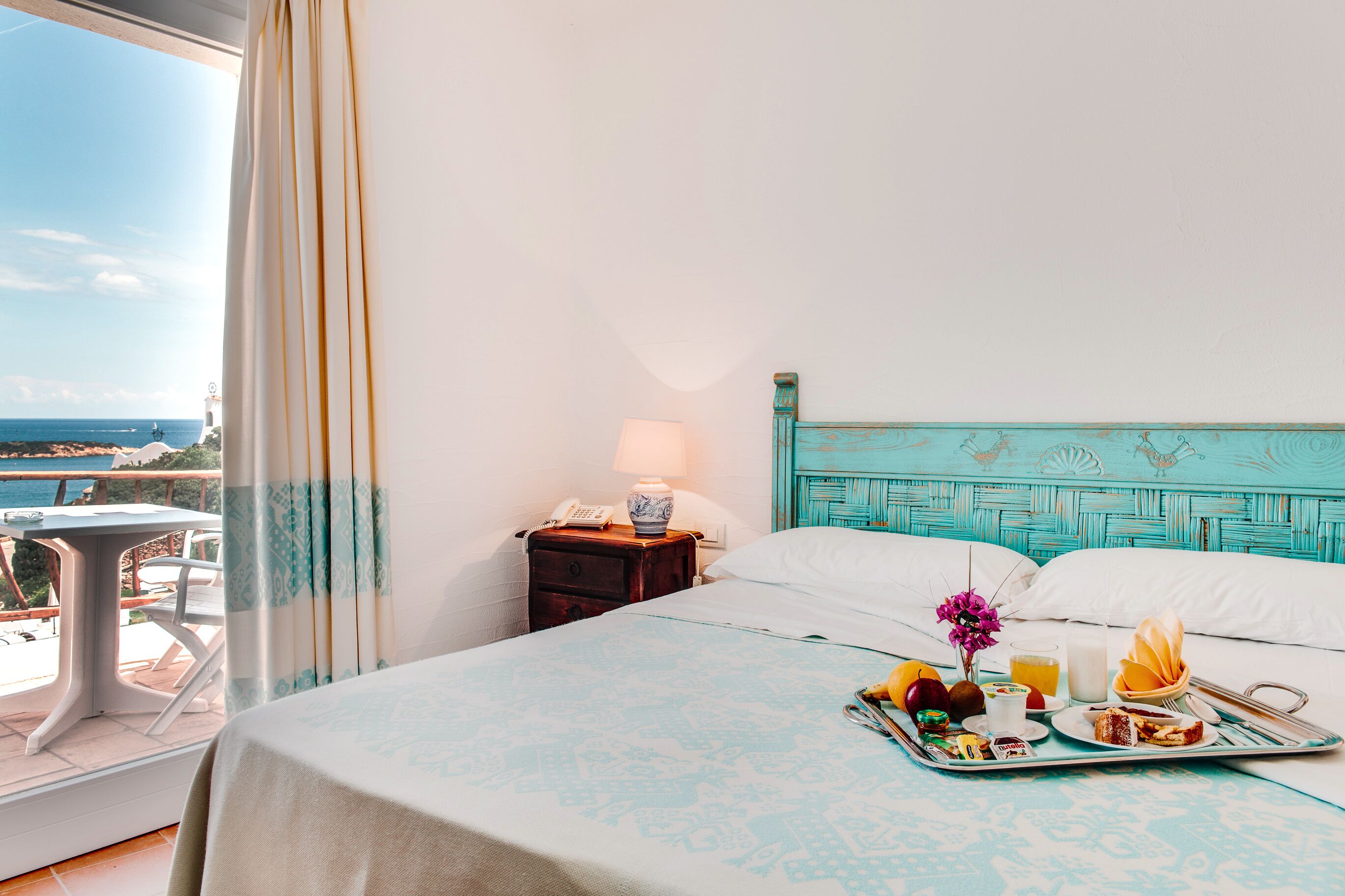 A hotel room with a bed, breakfast tray, and a view of the sea.