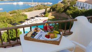 Een balkon met een eettafel en uitzicht op de kust, compleet met een mand eten, een glas sap en een banaan.