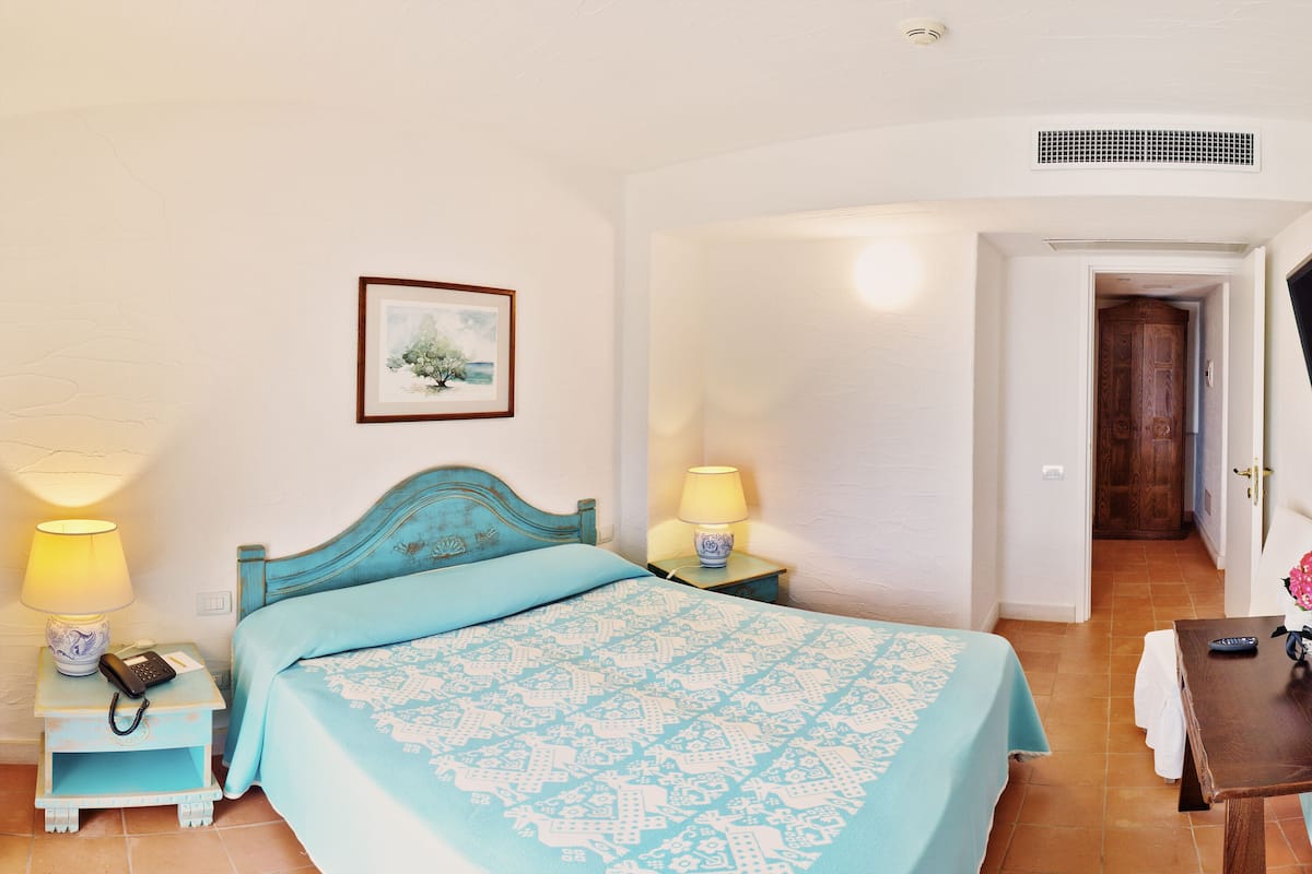 A bedroom with a bed, bedside tables, a lamp, a framed picture, and a door leading to another room.