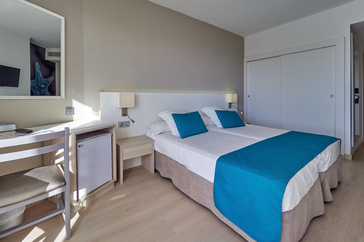 Una habitación de hotel con cama, mesitas de noche, escritorio y una silla.