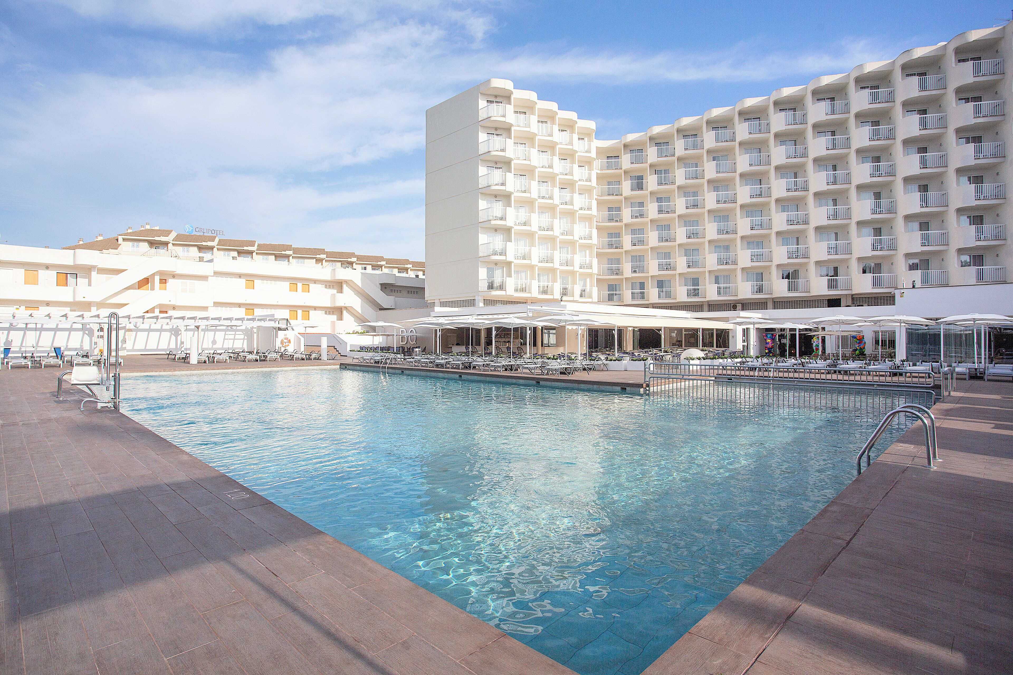 Un hotel con una piscina grande, varios balcones y zonas de estar al aire libre.