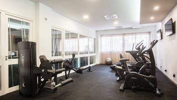 A modern gym with cardio machines, weight equipment, and large windows with curtains.