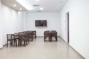 Una sala de conferencias con un televisor de pantalla plana montado en la pared, rodeada de mesas y sillas de madera.