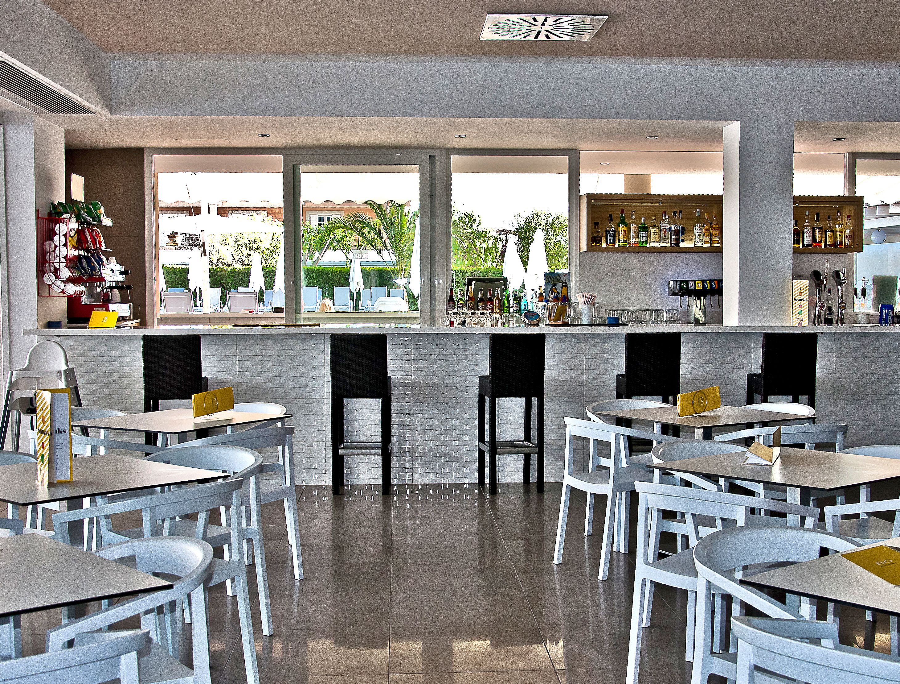 Un área de bar moderna con vistas al exterior, que incluye una barra, un espacio de estar y una variedad de botellas y vasos.