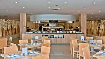 Un restaurante moderno con una barra central, varias áreas de estar y un techo alto con iluminación empotrada.