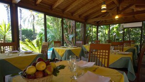 A restaurant with tables set for dining, a basket of fruit, and a view of tropical vegetation. - Hotel Borgo Verde (Catania)