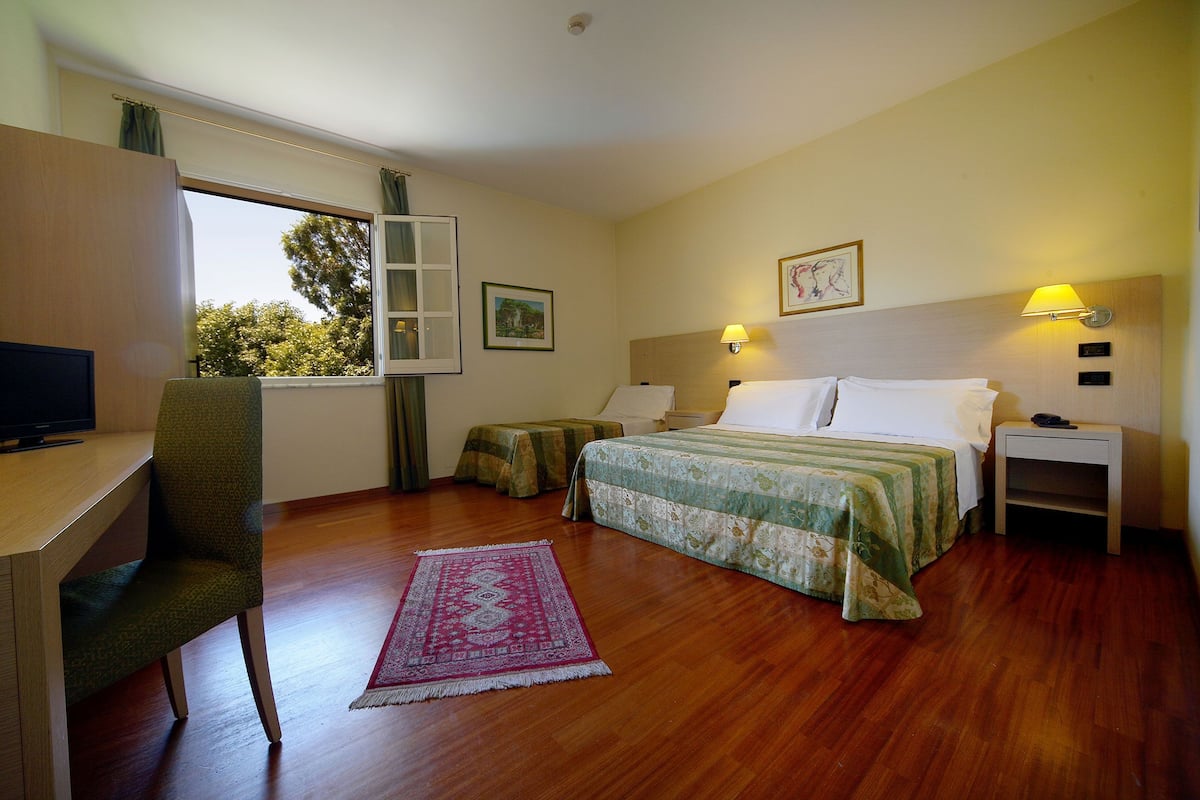 A hotel room with a bed, bedside tables, a desk with a chair, a television, and a window with curtains.
