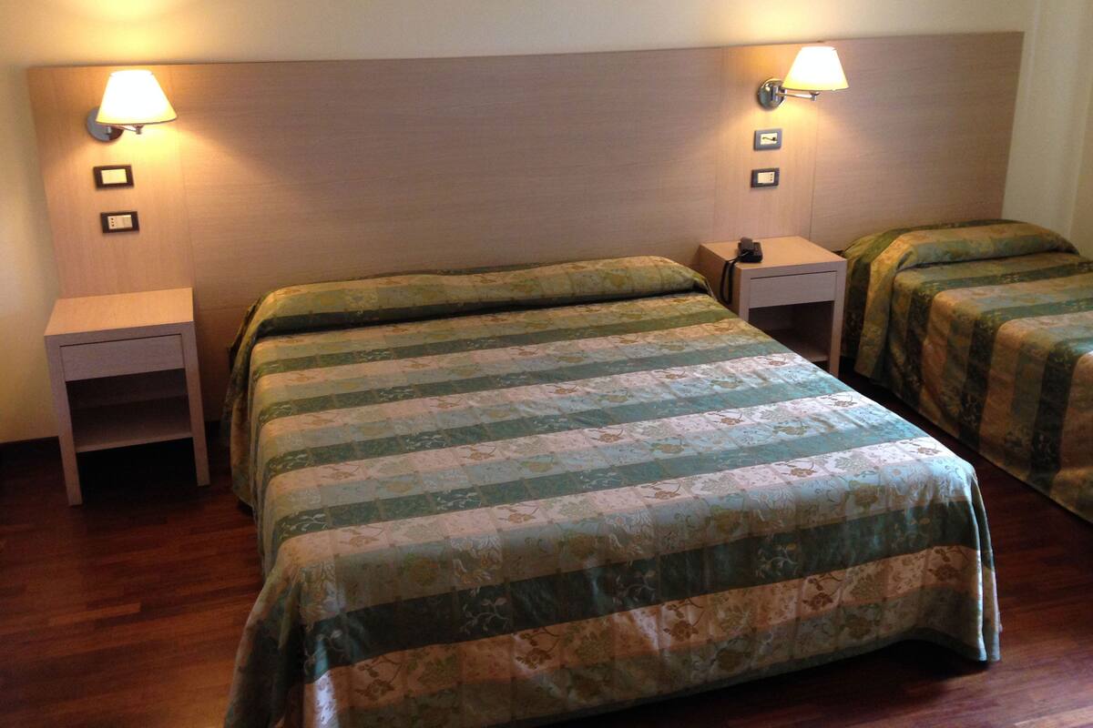 A hotel room with two beds, each with a floral-patterned bedspread, two bedside tables with lamps, and a wooden headboard.