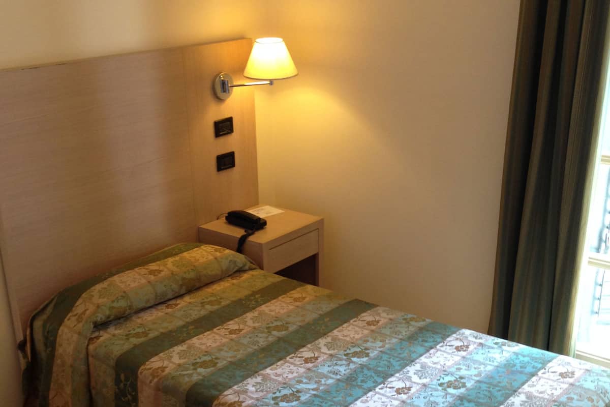 A hotel room with a bed, a nightstand, a lamp, and a telephone.