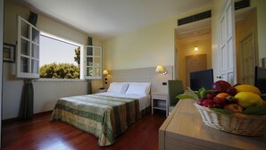 A hotel room with a bed, bedside lamps, a window with curtains, a desk with a fruit basket, and a television. - Hotel Borgo Verde (Catania)