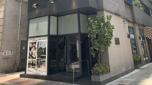 A modern building with a glass entrance, a signboard, and a staircase leading to the entrance.