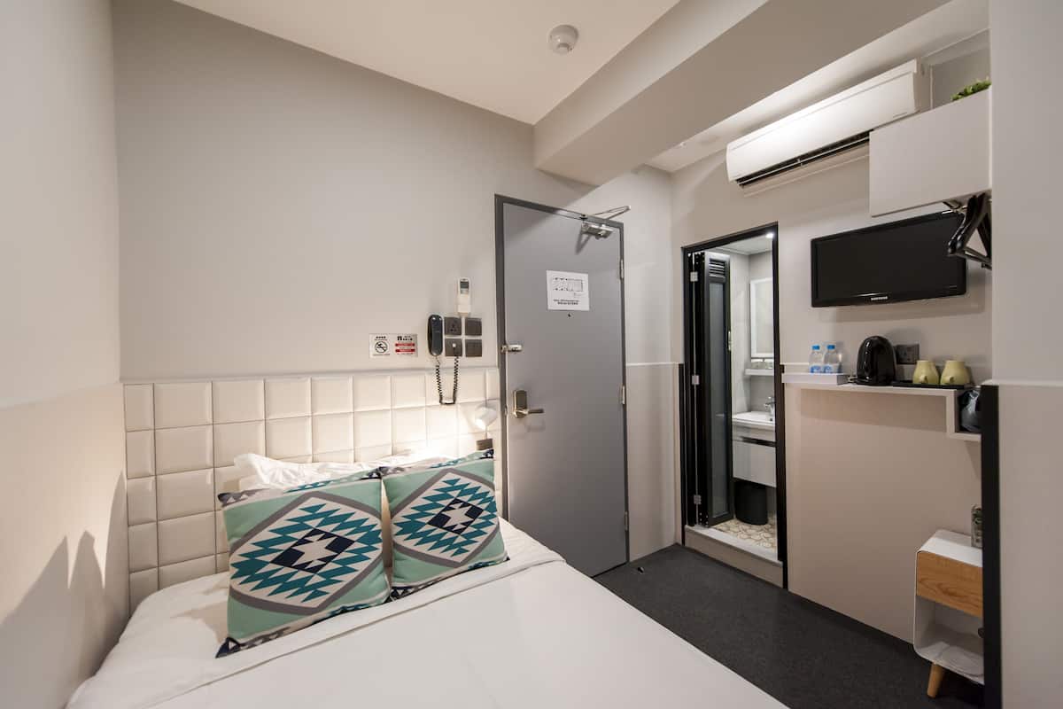 A hotel room with a bed, a door, a television, and a small kitchenette.