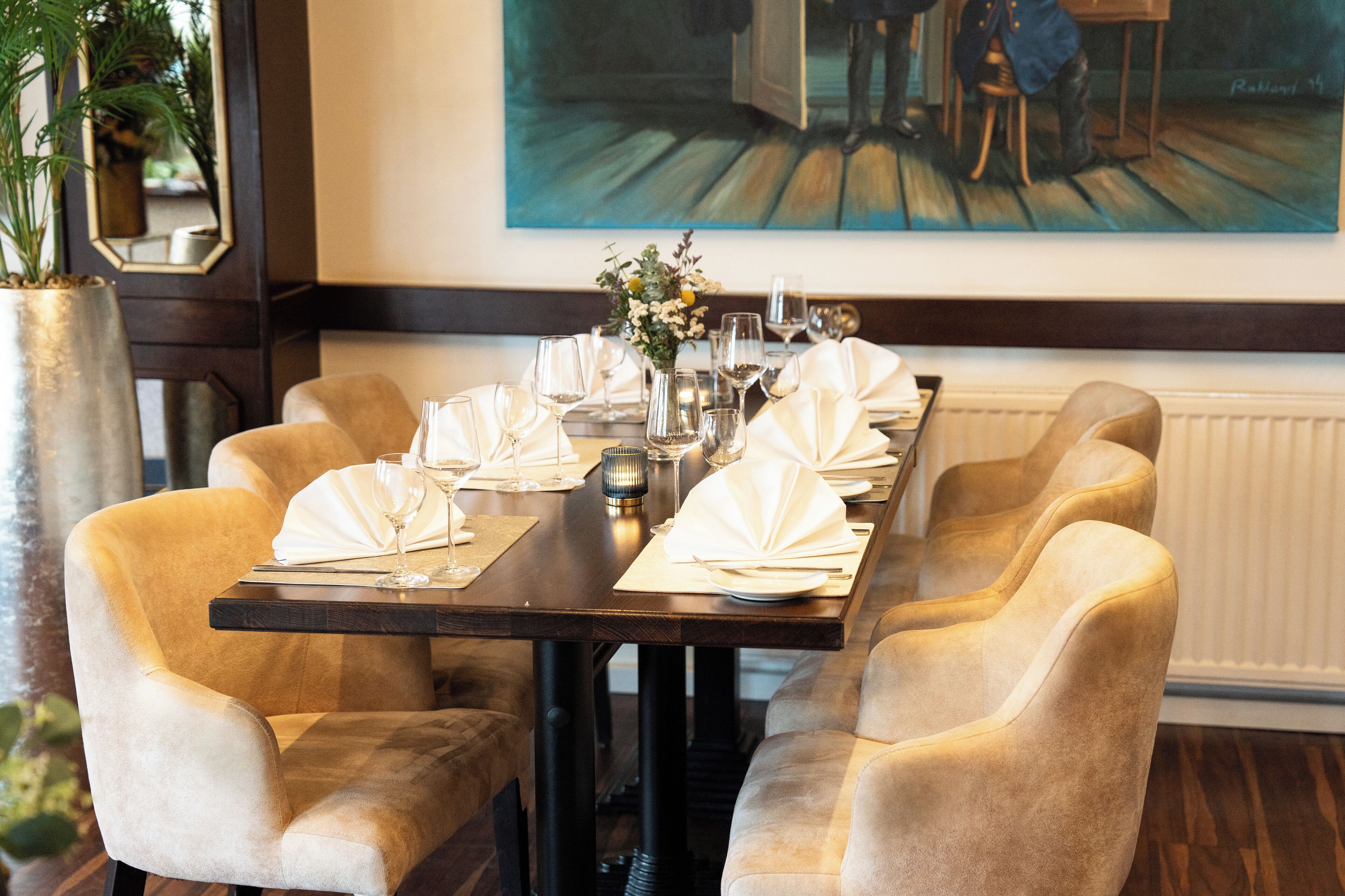 A dining table set for six with a vase of flowers, wine glasses, and a painting on the wall.