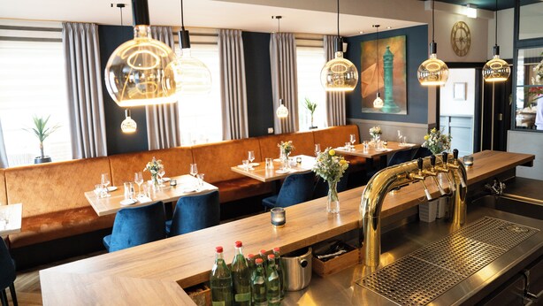 A restaurant with wooden tables, blue chairs, and hanging pendant lights.