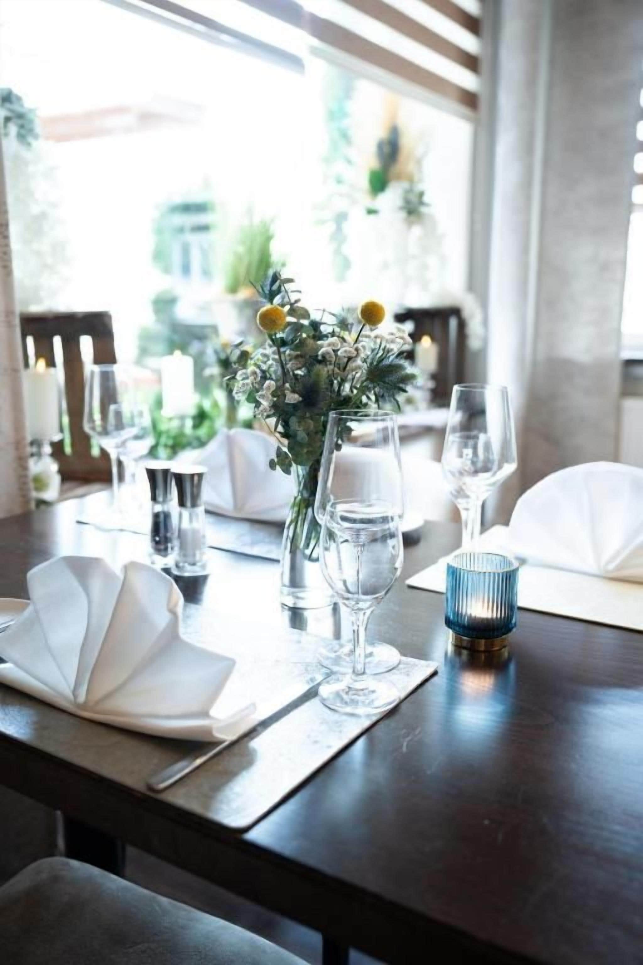Una mesa de comedor dispuesta con servilletas blancas, cristalería y un centro de mesa con flores.