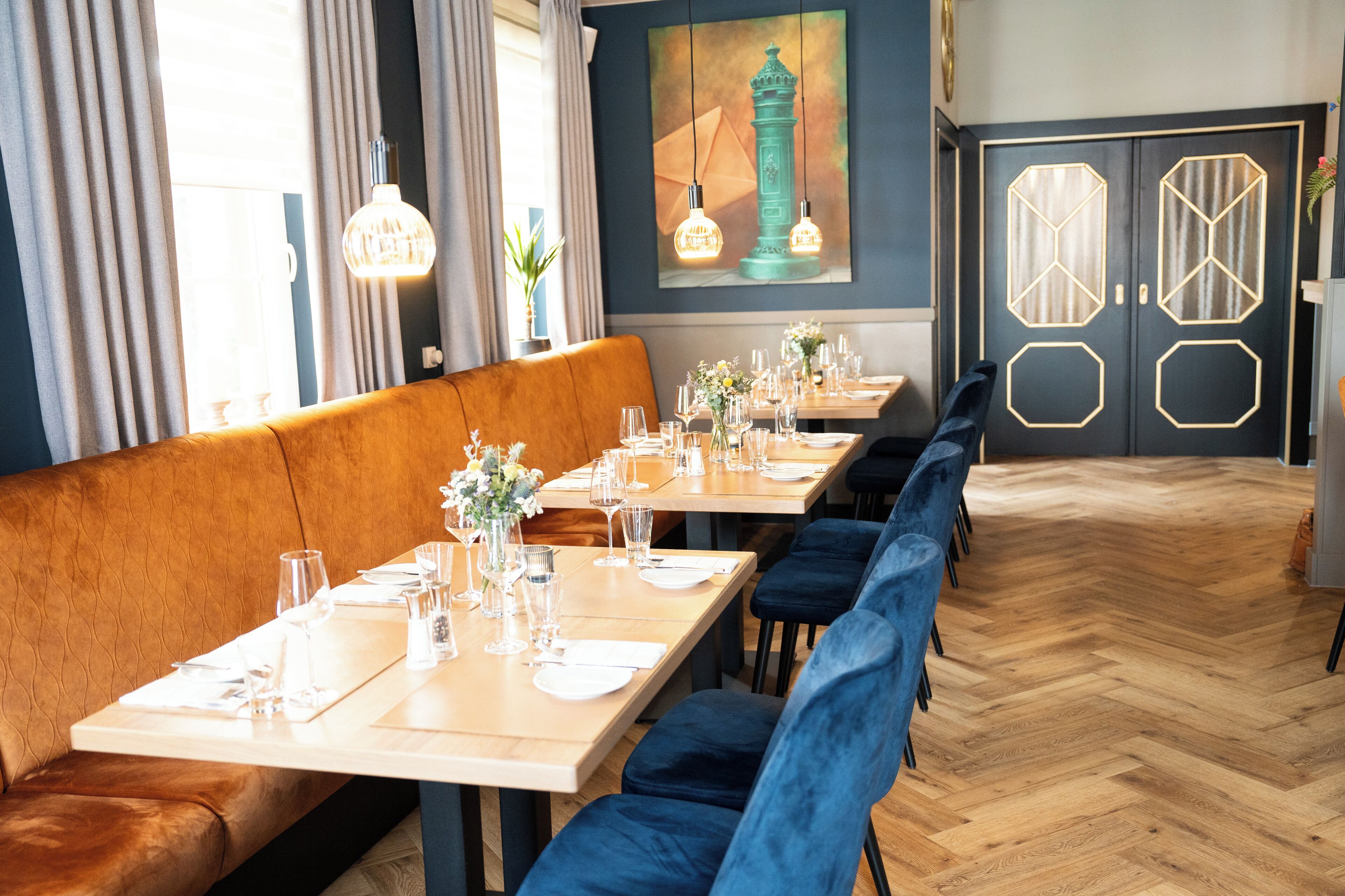 Un restaurante con mesas de madera, sillas de terciopelo azul y suelo con motivo de espiga.