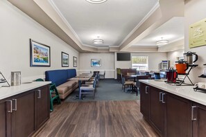 A hotel room with a kitchenette, a seating area with a sofa and chairs, and a dining area with tables and chairs.
