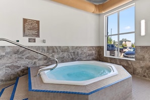 Una bañera de hidromasaje con una escalera metálica, un cartel con los horarios de uso del jacuzzi y vistas a coches aparcados a través de una ventana.