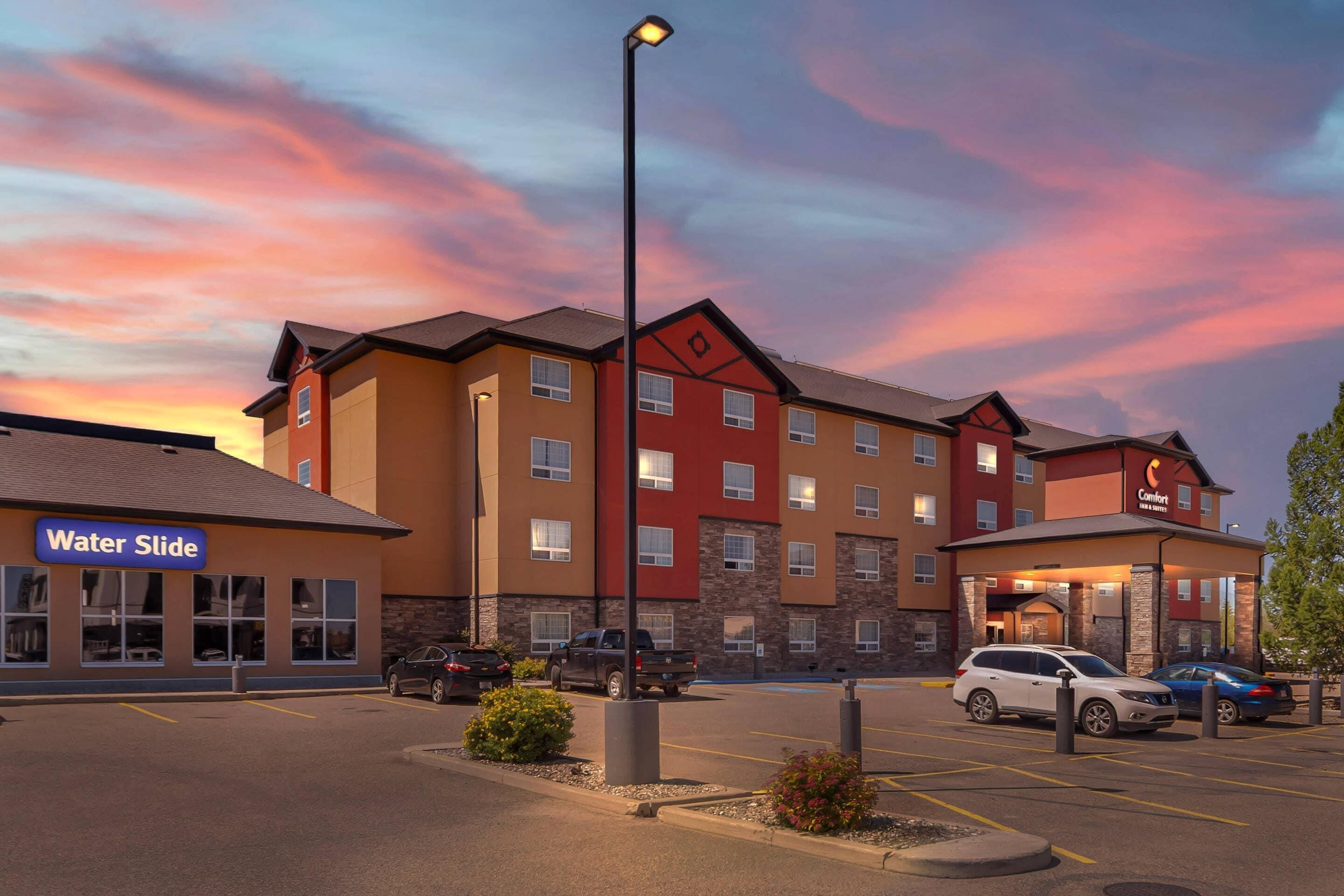 Un hôtel à plusieurs étages, avec une enseigne bien visible indiquant « Comfort Inn & Suites », un parking où sont garées plusieurs voitures et un lampadaire.