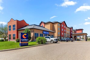A Comfort Inn & Suites hotel with a modern design, featuring a parking lot and a clear blue sky.