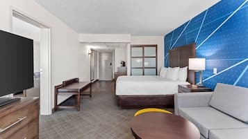 A hotel room with a bed, a sofa, a desk, a TV, and a bathroom.