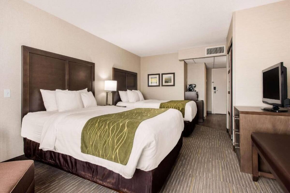 A hotel room with two beds, a desk, a television, and a door leading to another room.