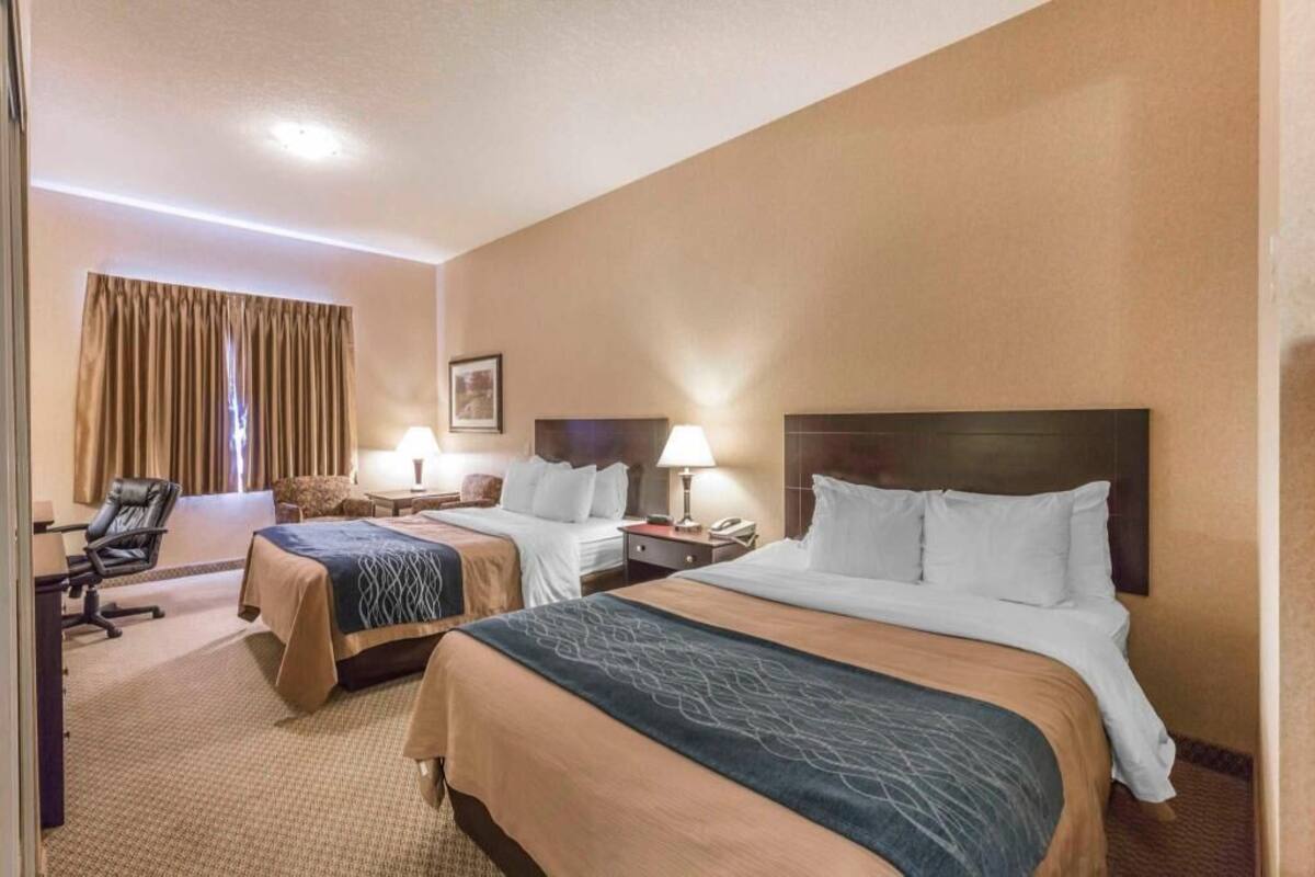 A hotel room with two beds, a desk, a chair, and a window with curtains.