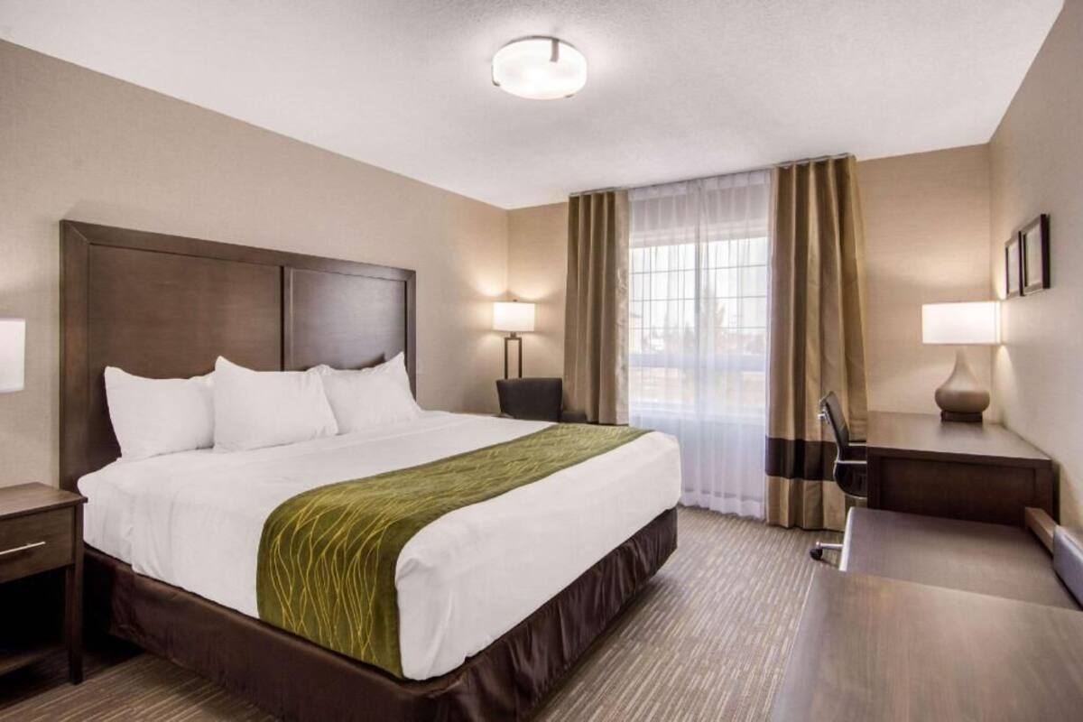 A hotel room with a large bed, bedside tables, a desk, and a window with curtains.