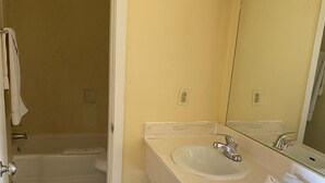 A bathroom with a bathtub, two sinks, a mirror, and a trash bin.