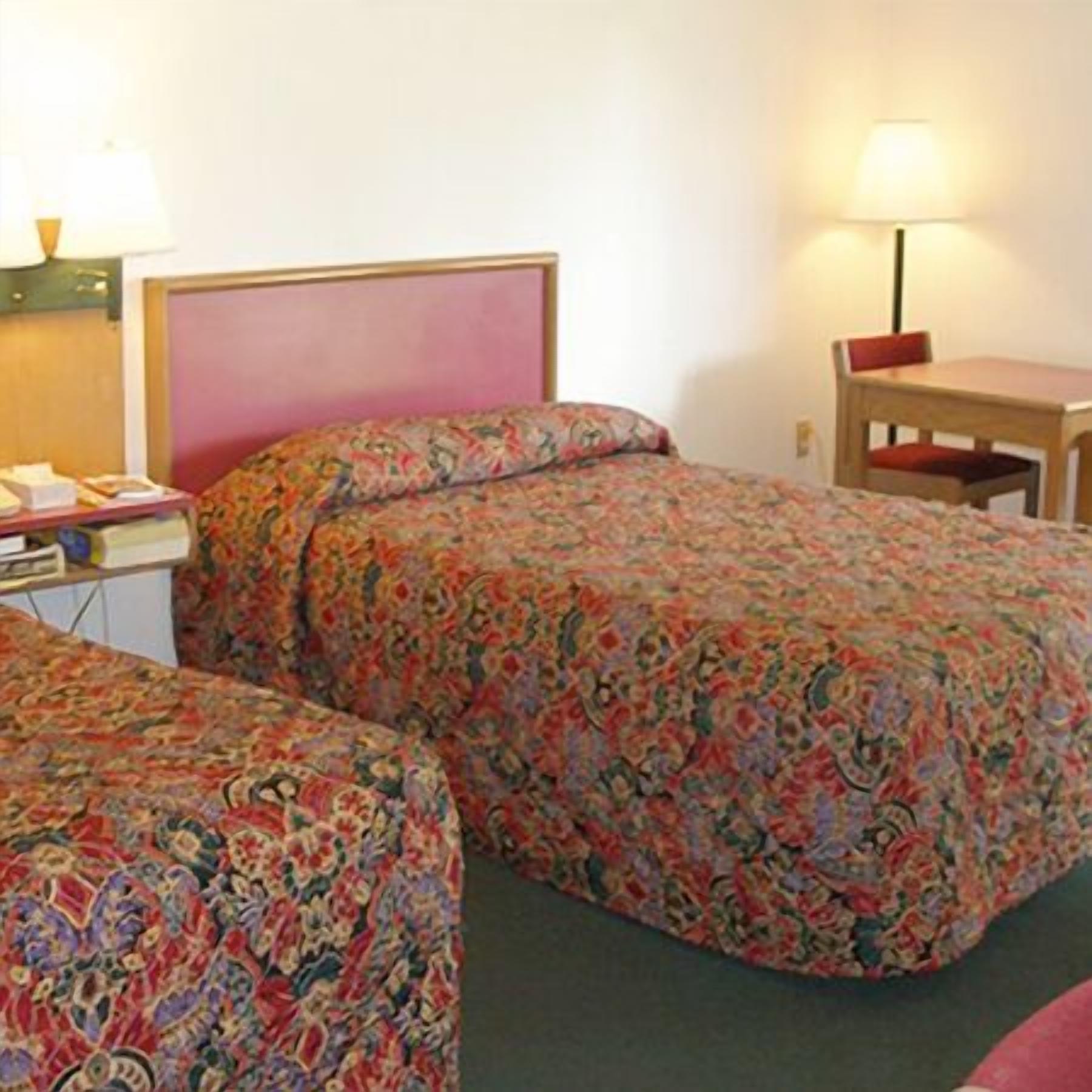 A hotel room with two beds, a desk, a chair, and a lamp.