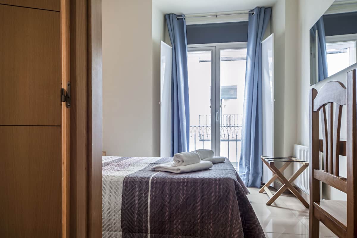 A bedroom with a bed, a wooden wardrobe, and a balcony with blue curtains.