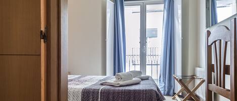 A bedroom with a bed, a wooden wardrobe, and a balcony with blue curtains.