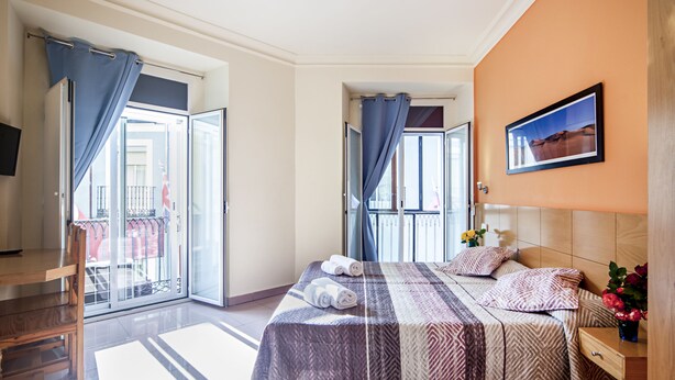 A hotel room with a bed, a desk, and a view of the outside balcony. - INTER Puerta del Sol - Auto Check-in (Madrid)