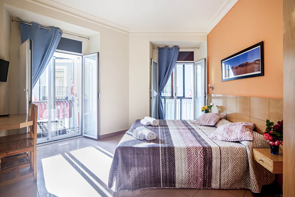 A hotel room with a bed, a desk, and a view of the outside balcony.