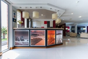 Una moderna recepción con un mostrador central, ventanas amplias y cuadros enmarcados de paisajes costeros.