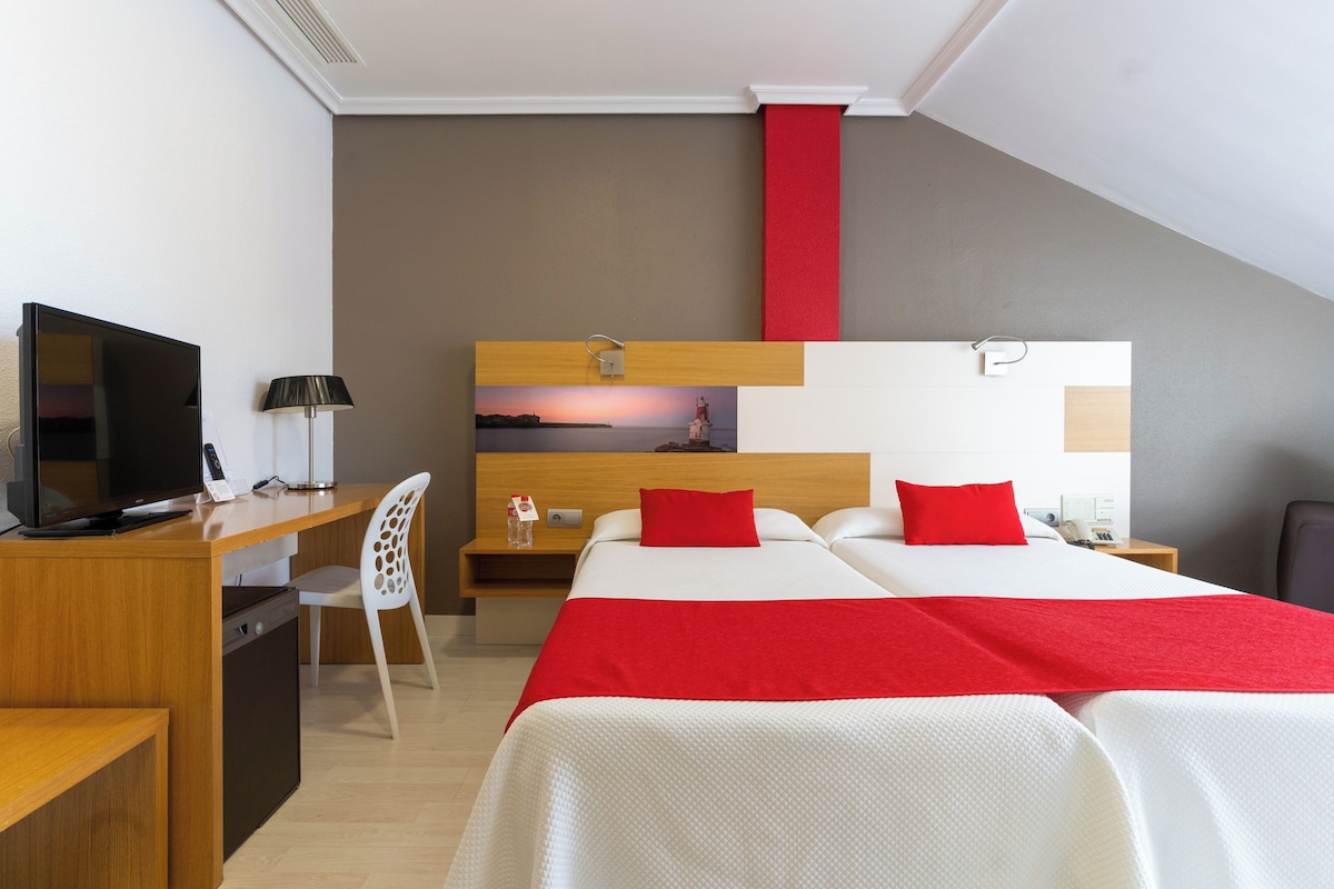 Une chambre d’hôtel comprenant un lit, un bureau avec une télévision, une chaise et une table de chevet.