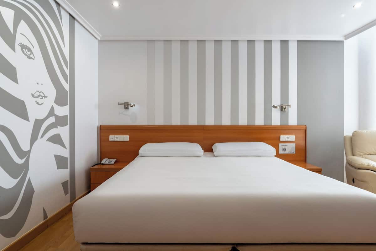 A hotel room with a large bed, wooden headboard, bedside tables, and a chair.