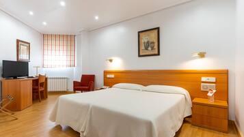 A hotel room with a bed, bedside tables, a desk with a chair, a television, and a window with curtains.