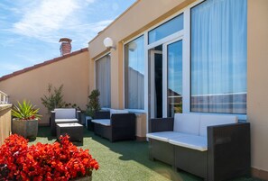 Un patio al aire libre con mobiliario de mimbre, plantas en macetas y vistas del exterior del edificio.