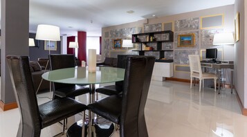 Una sala de estar moderna con una mesa de comedor de vidrio rodeada por sillas negras, un sofá blanco y una pared de acento roja.