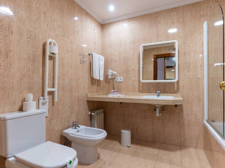A modern bathroom with a toilet, bidet, sink, and mirror.
