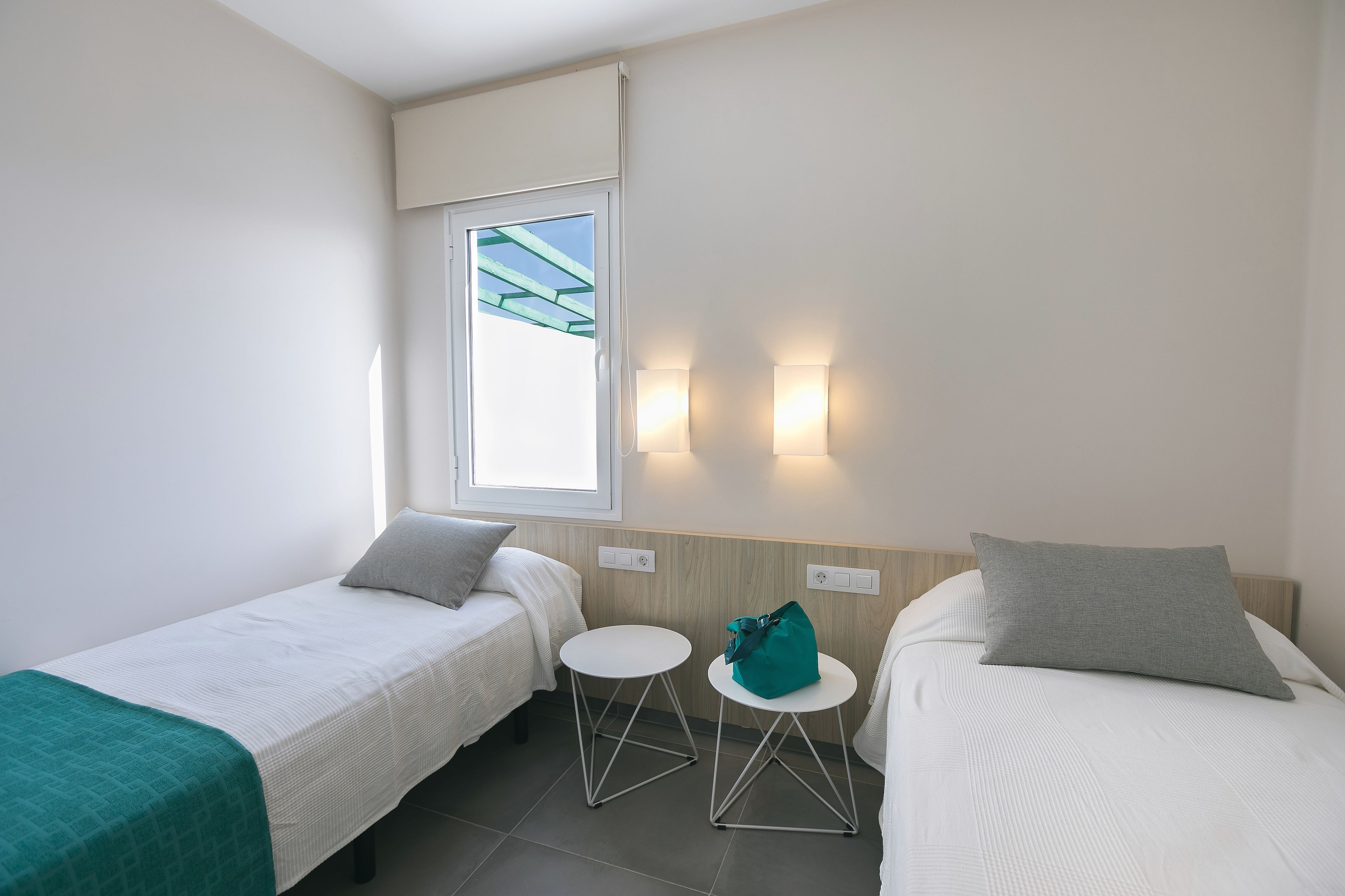 Una camera d'albergo con due letti singoli, un tavolino rotondo, una finestra con tende e illuminazione a parete.