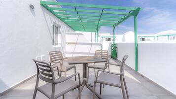 Een terras met tafel en stoelen, een groene pergola en witte muren.