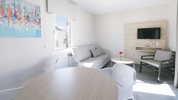 En moderne stue med sofa, spisebord og et fjernsyn ophængt på væggen.