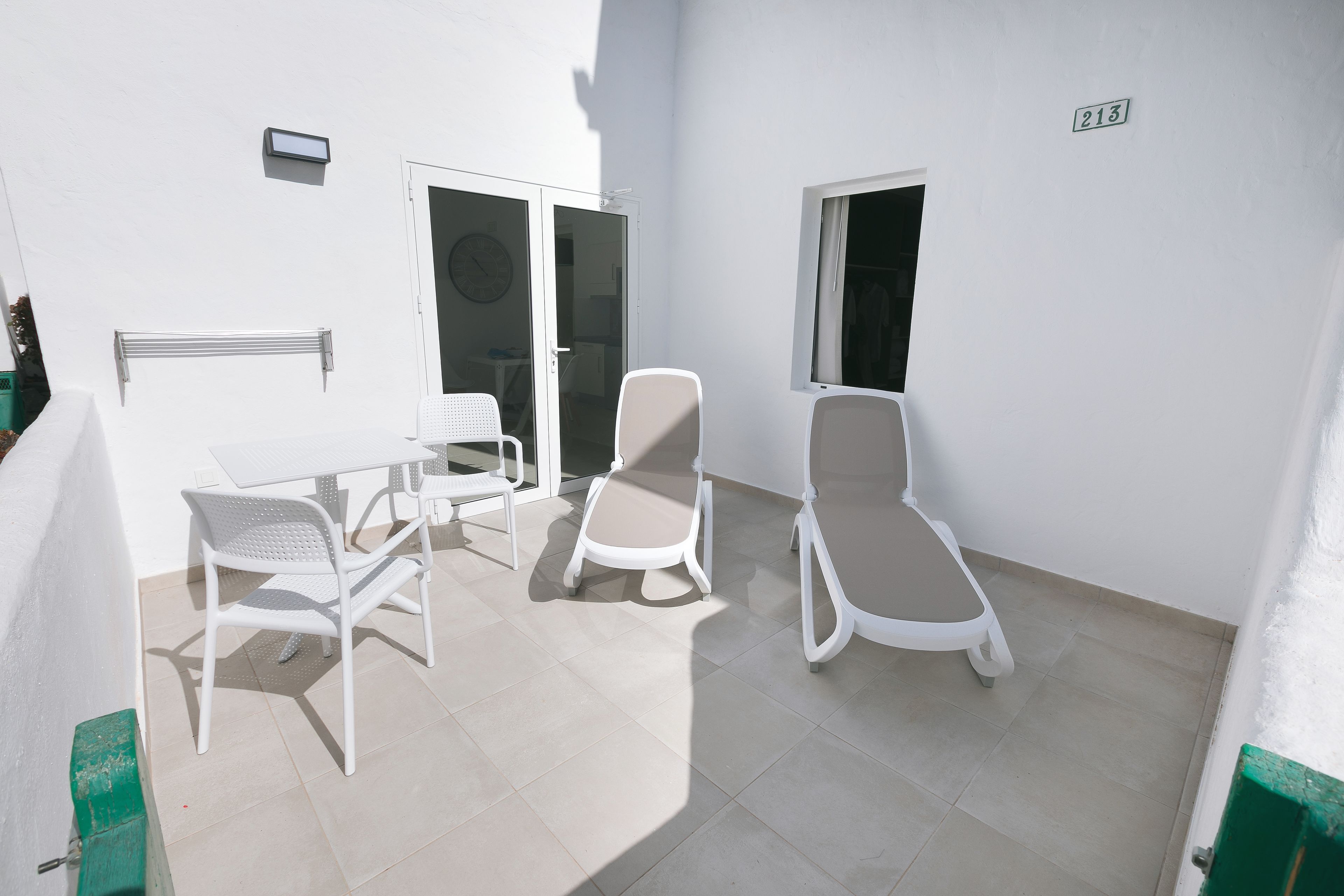 Un patio con sillas y mesa blancas, una puerta corrediza de vidrio y una ventana con el número.