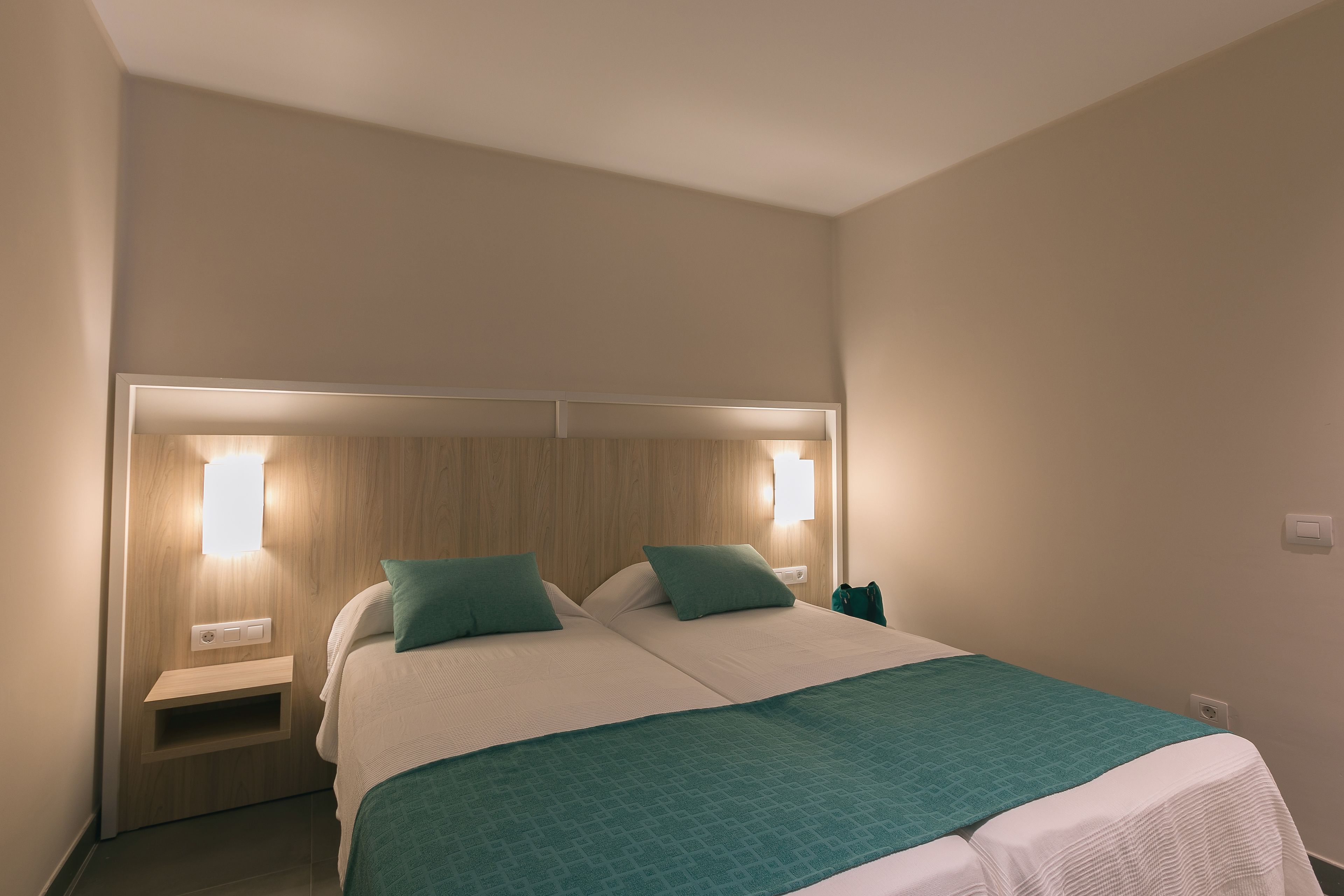 A hotel room with a large bed, two bedside tables, and wall-mounted reading lights.
