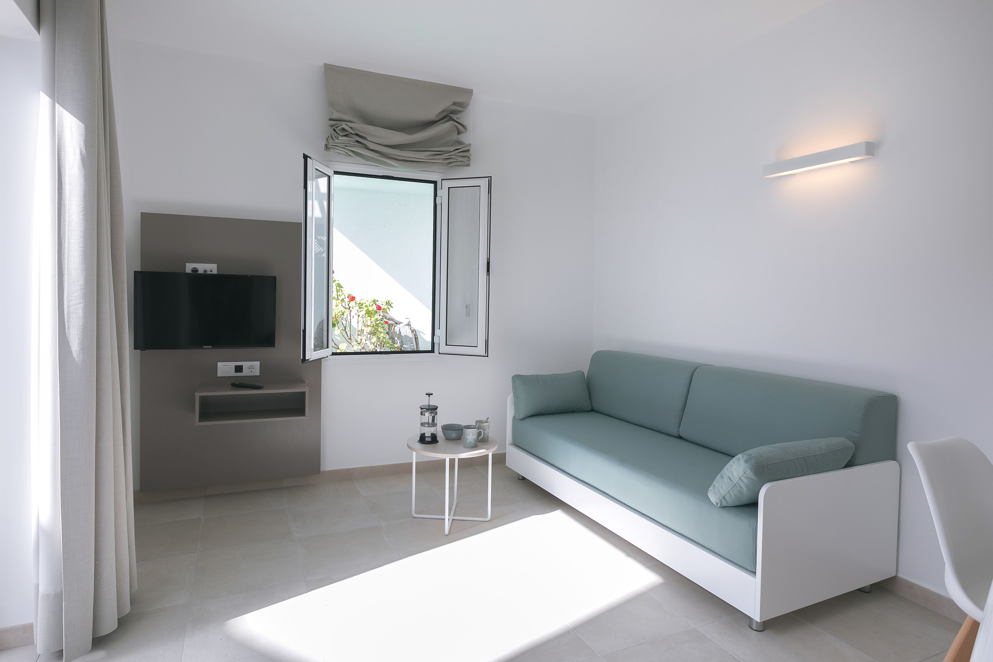 A modern living room with a sofa, a small table, a flat-screen TV, and a window with curtains.