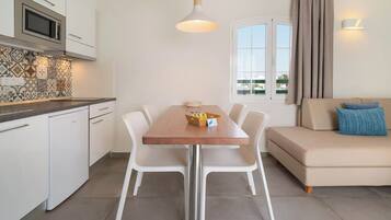 Une cuisine moderne avec des meubles blancs, un four à micro-ondes et un coin repas comprenant une table et des chaises en bois.